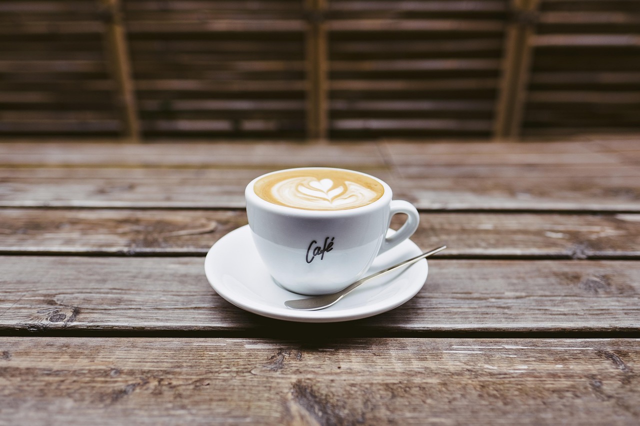 A latte with leaf art in a cup on a saucer, on a rustic wooden table